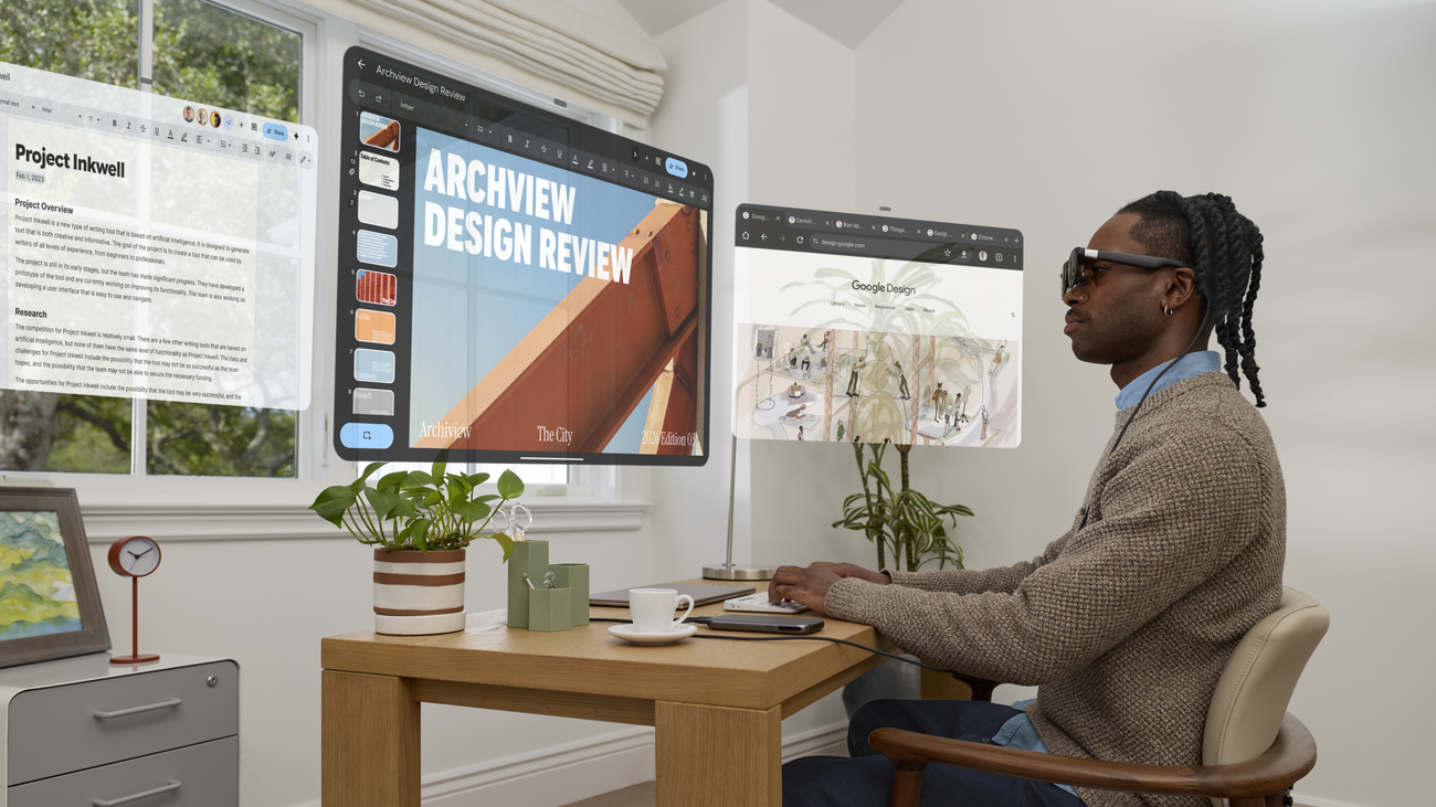 A man in dark glasses sits at a desk with several floating app windows, including a design review slide, in front of him