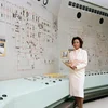 Photograph of mathematician Annie Easley, holding a clipboard and standing in front of a switchboard.