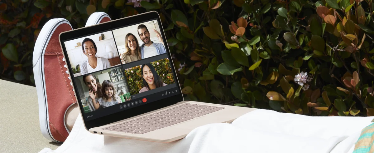 A laptop sitting on a person’s legs displays a video call with a group of people.