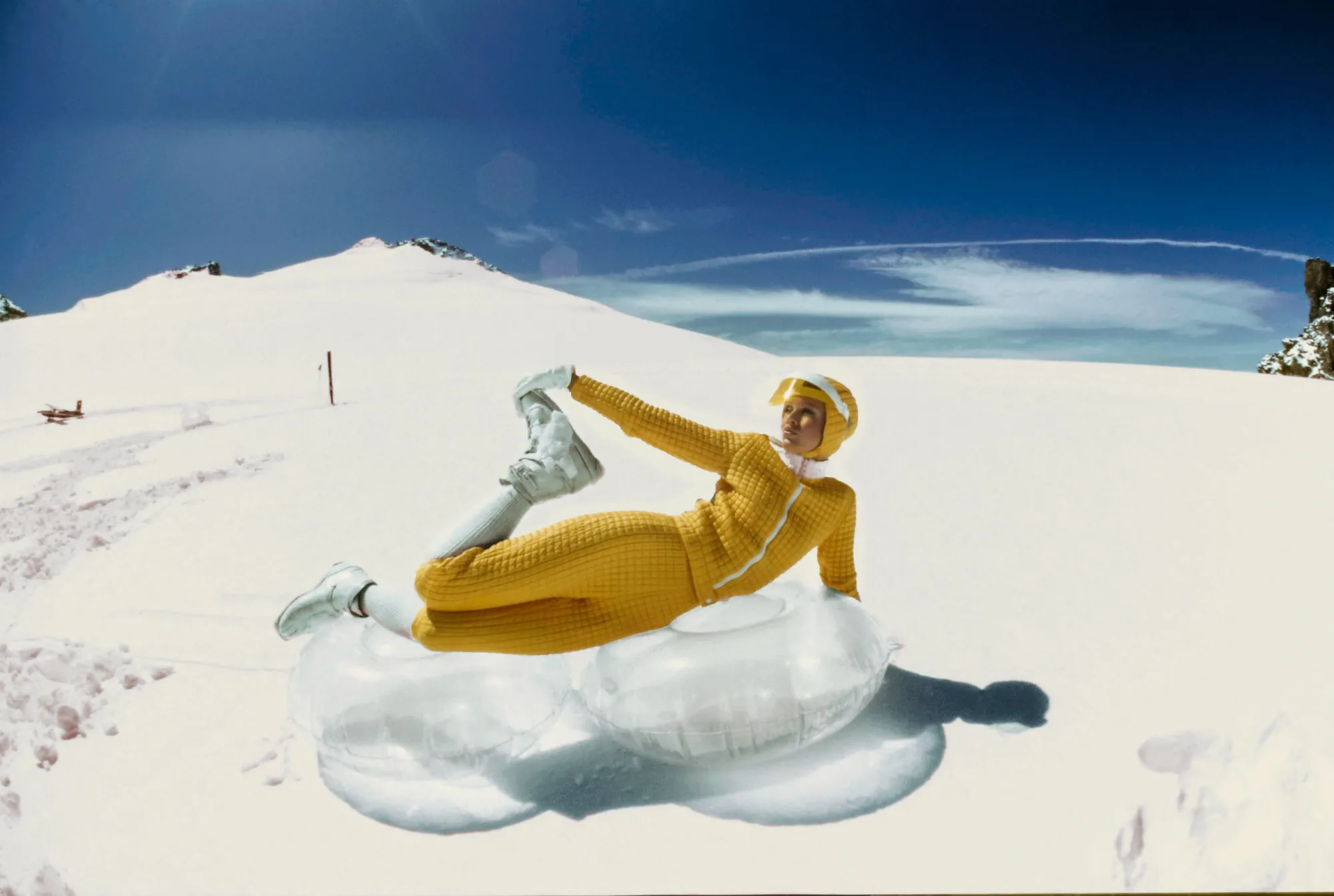 A model poses in the snow at the top of a mountain wearing a bright yellow outfit