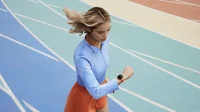 Image d'une femme courant sur une piste. À droite, vue rapprochée de l'entraînement au rythme sur la Pixel Watch 2 avec le bracelet Coral Active Sport Band.