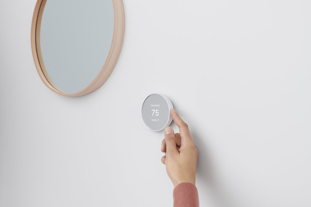 Image showing a hand adjusting a Nest Thermostat on a wall next to a circular mirror.