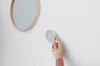 Image showing a hand adjusting a Nest Thermostat on a wall next to a circular mirror.