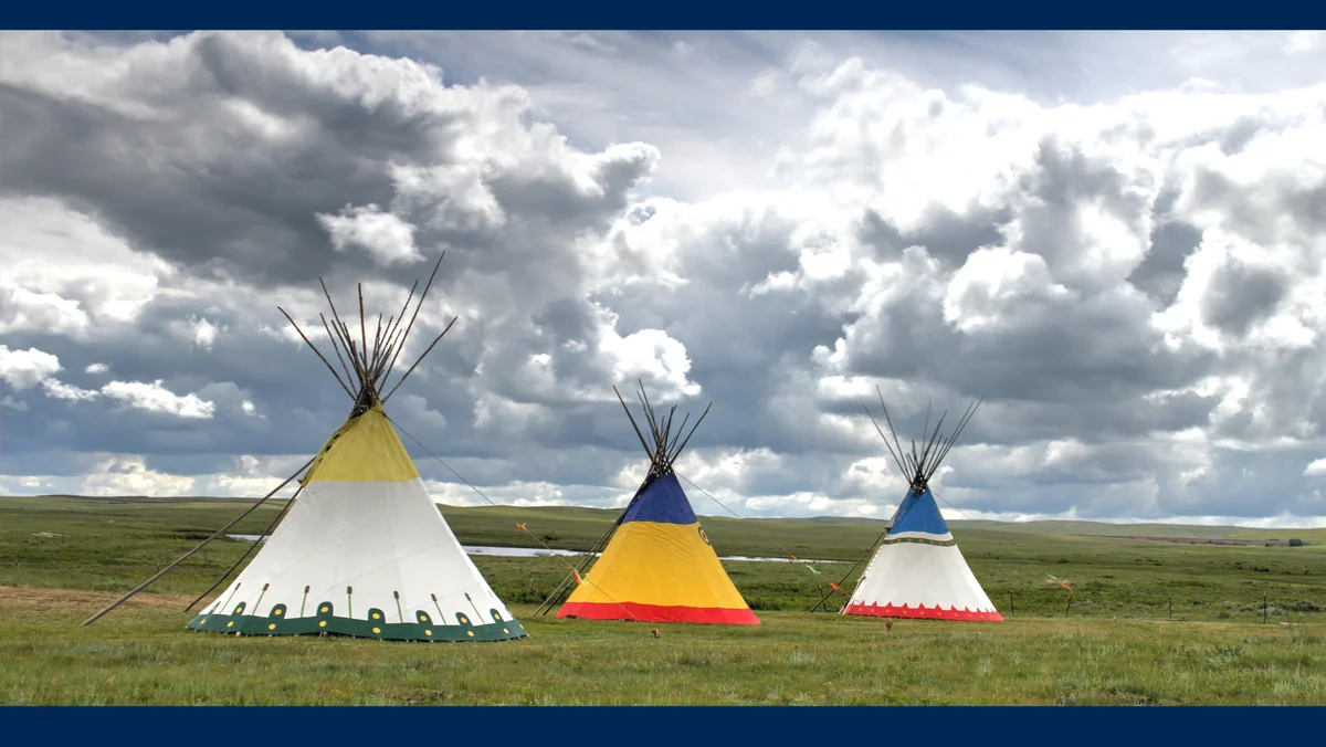 Three tipis stand against a stormy sky.