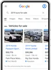Smartphone shows Search results for “2019 suvs for sale.” There are two ads, each showing a picture of a car and its details. The ad on the left shows a white SUV and the ad text below the image says “2019 Honda Passport Sport, $32,773, Used - 8k mi, Park Place Motors” and has a location icon to indicate the car is in Fort Worth, Texas. The ad on the right shows a dark blue SUV and the ad text below the image says “2019 Toyota RAV4 Limited, $35,286, Used - 16k mi, Big Star Honda” and has a location icon to indicate that the car is in Houston, Texas.