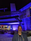 Image of a man in a grey hoodie standing in front of a building lit up with a purple light.