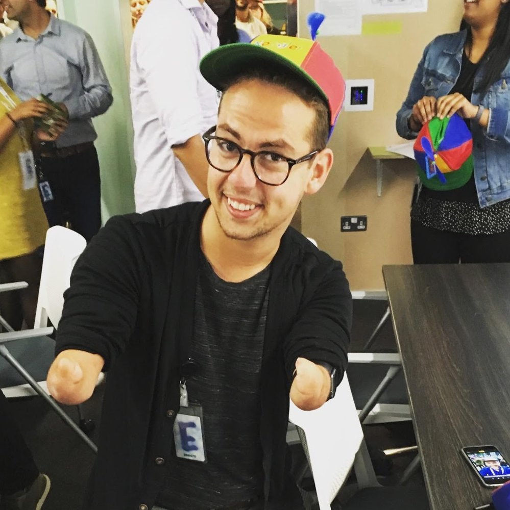 Patrick poses with a multicolored hat given to new Googlers at orientation. In the background are other new Googlers with their hats.