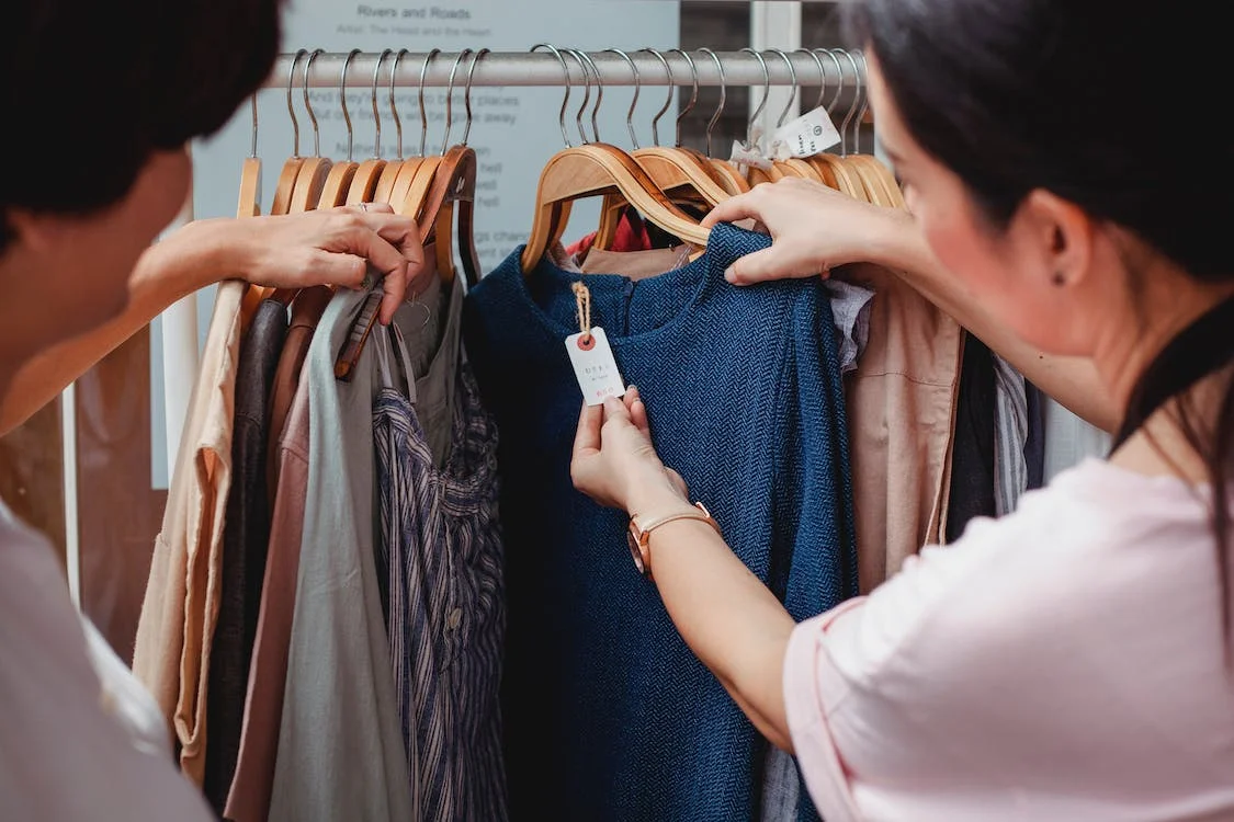 Two people look at items on a clothing rack, pausing to look at the price tag on a blue dress.