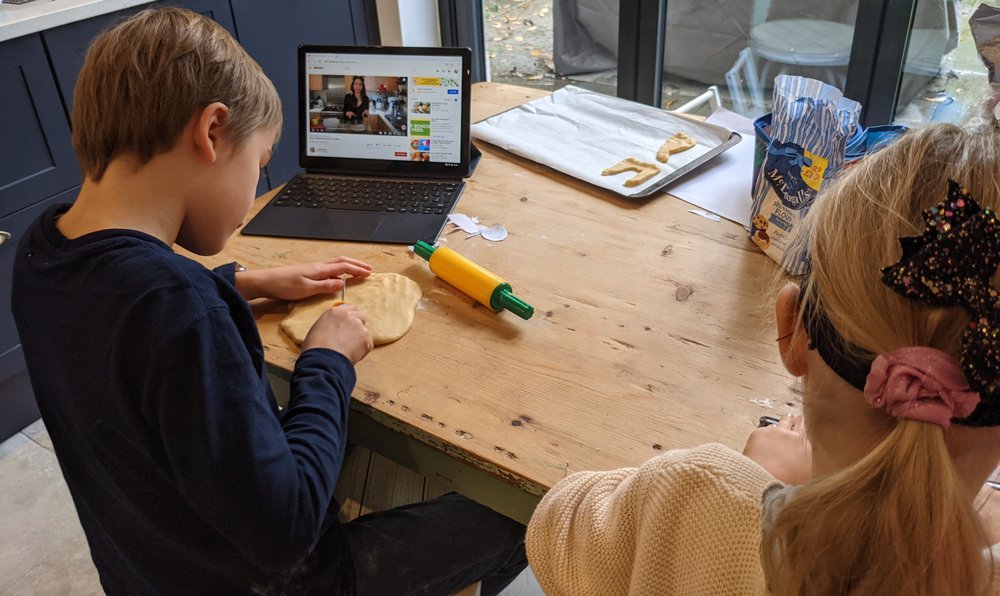 Two children roll out dough while watching an instructional video on YouTube