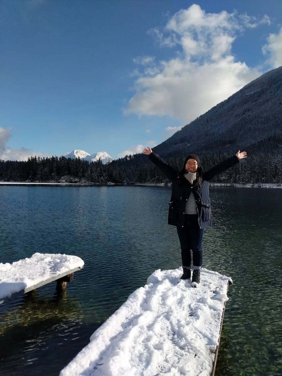 Marisa Chow steht auf einem schneebedeckten Steg vor einem See in Bayern