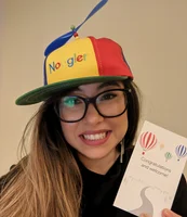 Ein Selfie Desi Nedelcheva. Sie trägt eine bunte „Noogler“-Mütze, lächelt in die Kamera und hält eine Karte in die Kamera auf der "'Congratulations and welcome" steht.