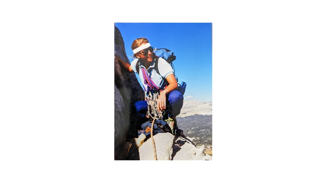 A woman stands on the cliff of a mountain with climbing gear.