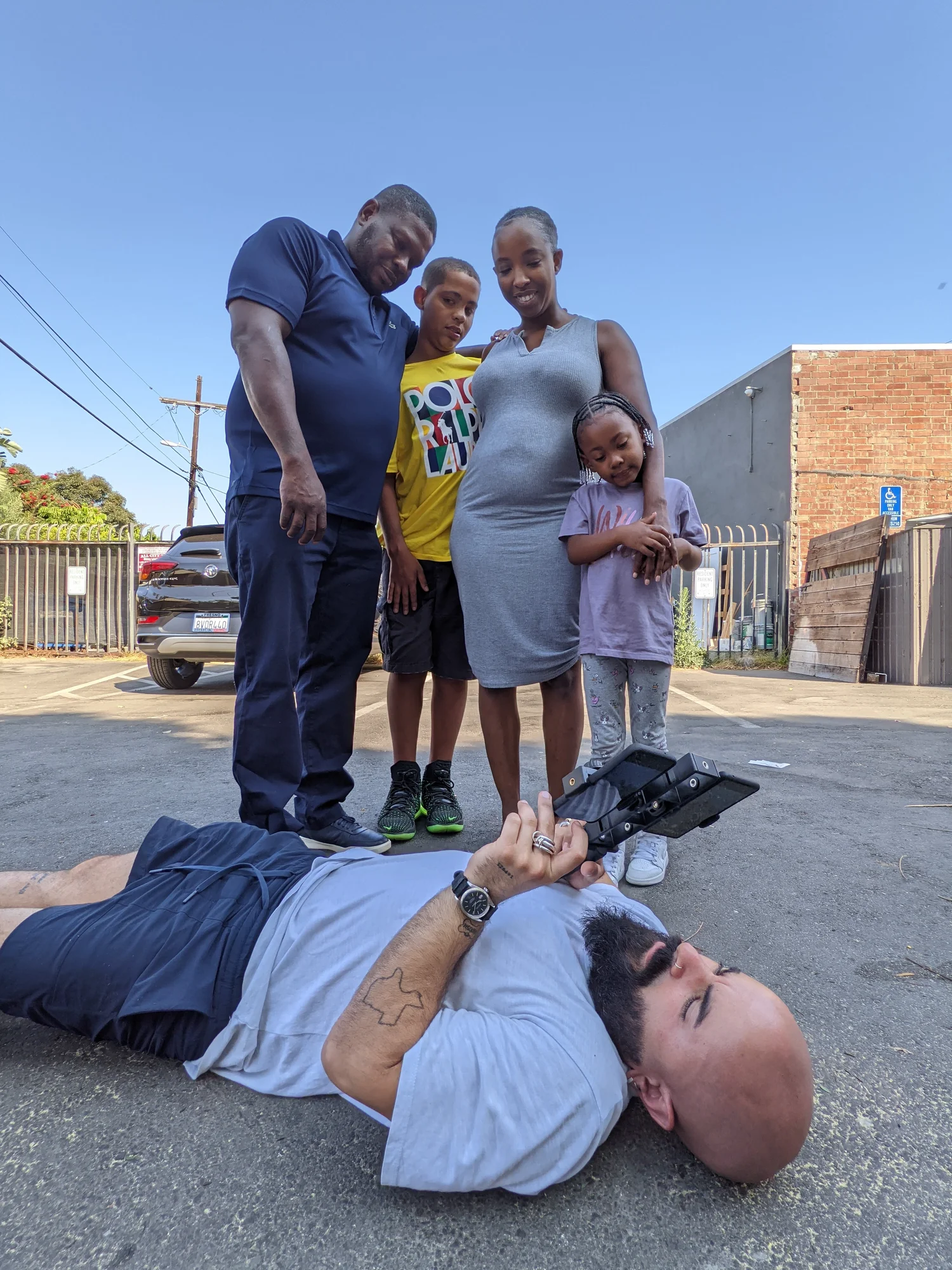 A photographer lays on the ground to take a portrait of a family of four from below.