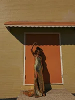 Photography of a woman in a gown posing against a brown wall outside.