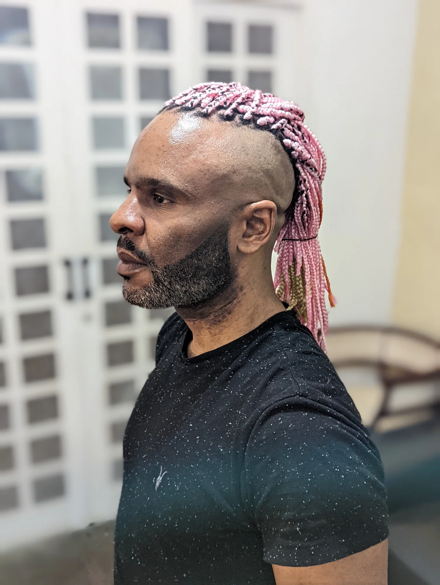 Seitliches Porträtfoto von Daniel Castro do Nascimento. Er steht vor einem Kleiderschrank, trägt ein schwarzes T-Shirt und seine Haare in pinker Farbe.