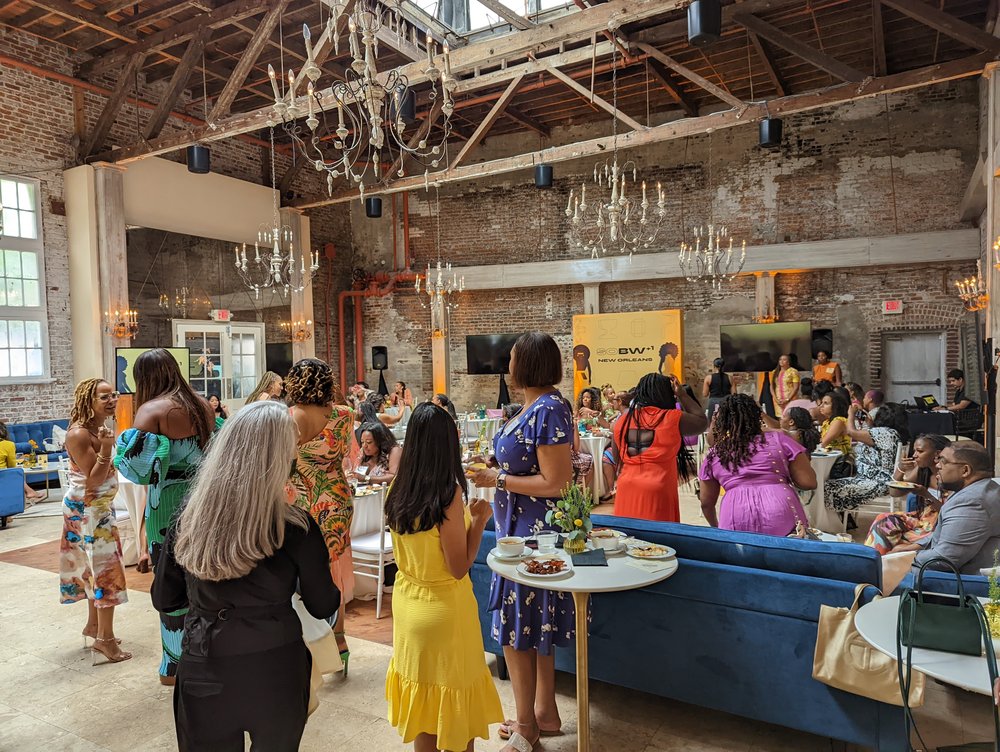 Attendees gather around tables and in seating areas in a warehouse space with chandeliers overhead.