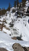 A photograph of a small river with snow on either side. The water is showing a blurry, motion effect.