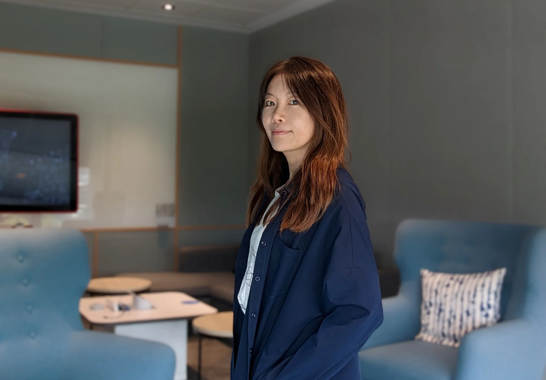 A close up of a person wearing a navy blue sweater in a room of blue couches, looking at the camera