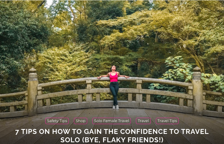 A woman in a bright pink tank top and jeans leans back against the stone railing of a bridge set in a forest.