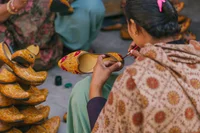 Color photograph of a person painting a pattern onto a leather shoe, surrounded by a pile of leather shoes.