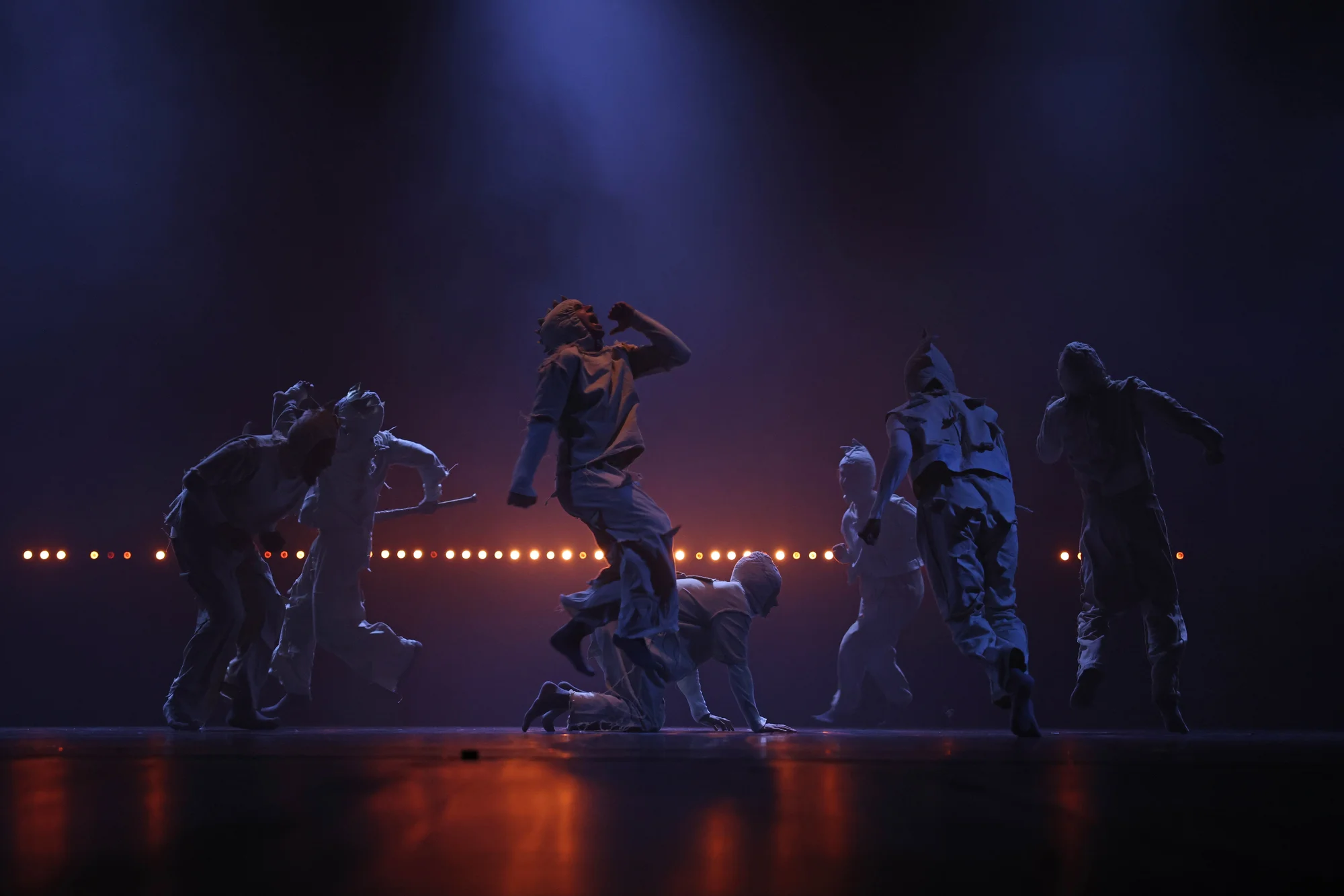 A still of a Far From The Norm performance, showcasing seven dancers on stage with lights behind them