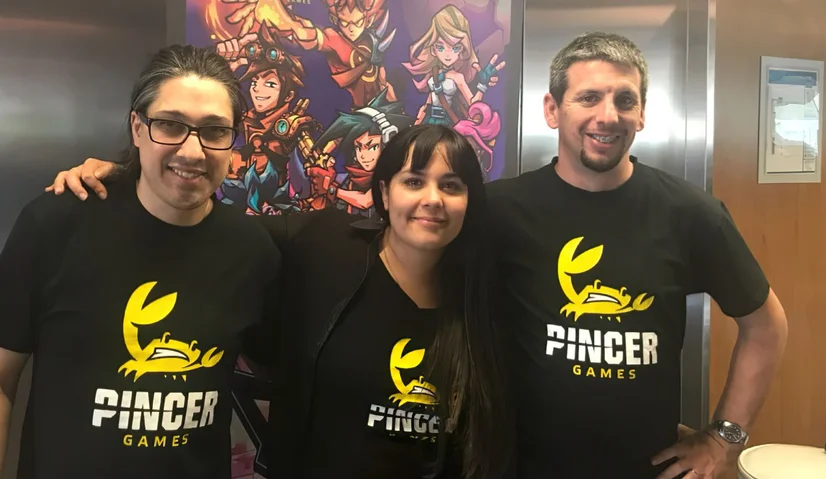 Three people wearing black t-shirts with the Pincer Games logo stand with their arms around each other.