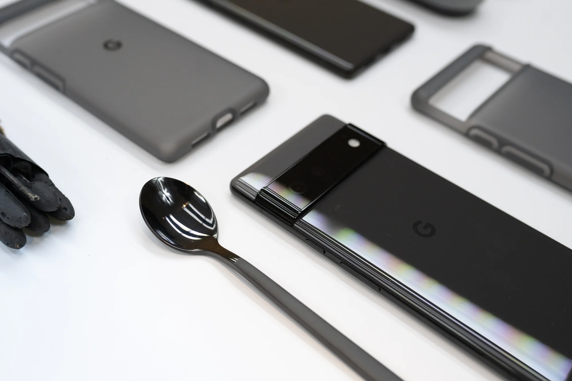 Photograph of the Stormy Black Pixel 6 next to the black case and various items in different shades of black, including a small, shiny black spoon.