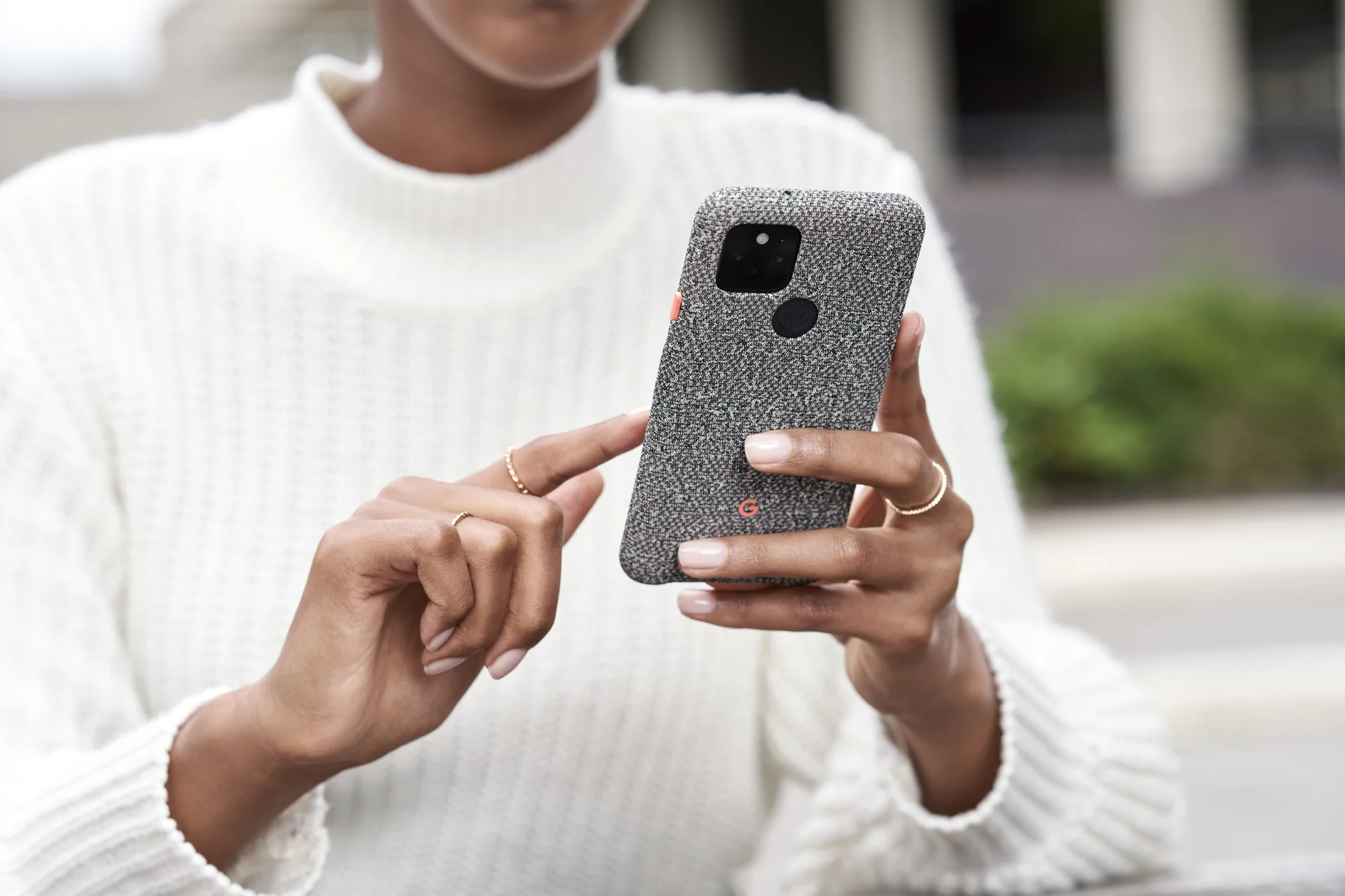 Image showing a woman wearing a white sweater holding a Pixel 5 in a blue case.