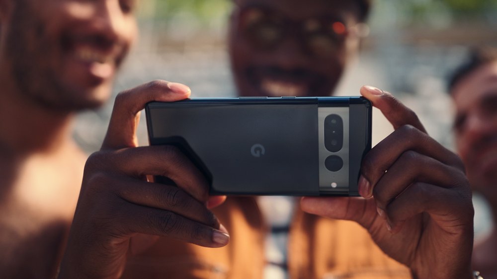 A person is holding a Pixel 7 taking a photo, two friends look at the screen next to them.