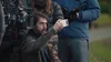 A bearded man sitting next to a cinema camera is holding a Pixel phone in front of his face