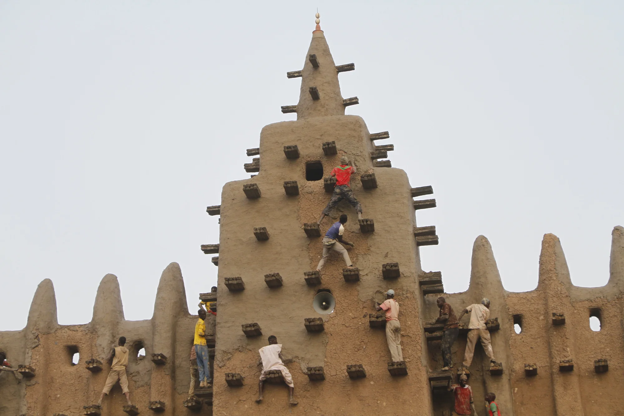 Local community members climb the Great Mosque of Djenne to replaster its facade in a festival.