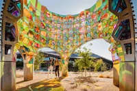 Photo of a piece of artwork this is a large kaleidoscope-like structure with two woman admiring the colors.