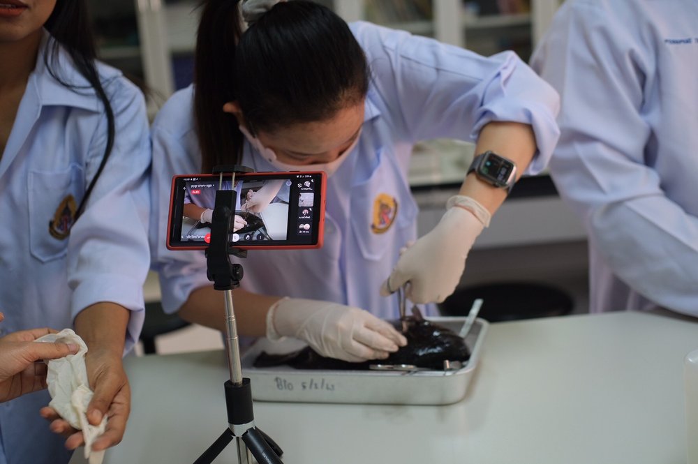 A close-up photo of a high school student working on a science experiment, there's a tripod holding a phone up as they work.
