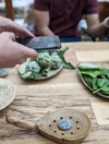 Persona toma fotografía de alcachofas y albahaca sobre una mesa con su teléfono móvil.