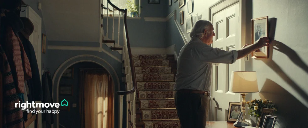 An older man hanging up a photo frame in what's depicting his new home