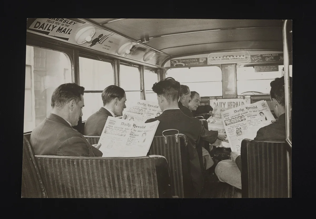 An old, black and white photograph of men on the bus, reading The Daily Herald newspaper.