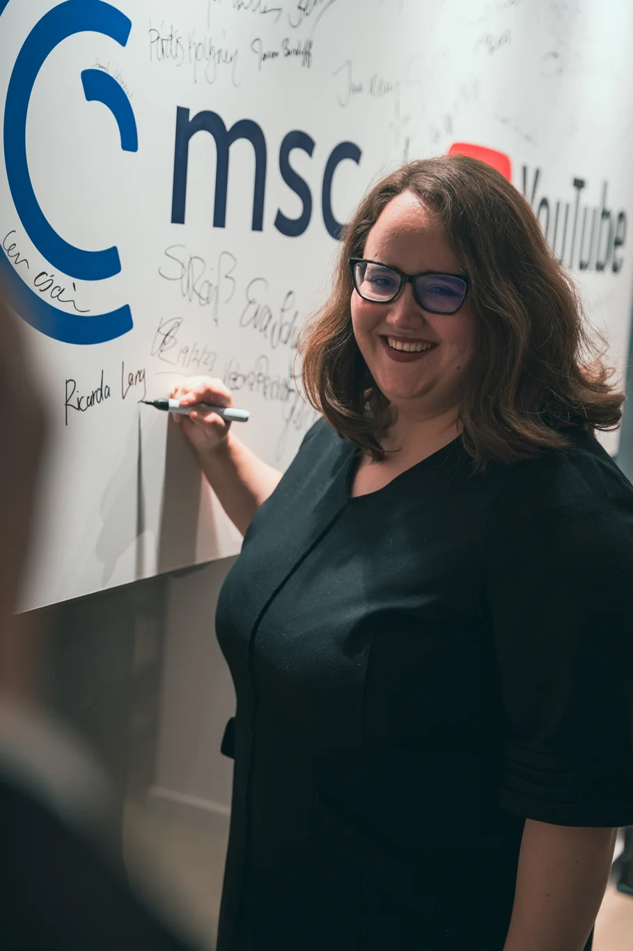 Frau lächelnd mit Stift in der Hand an der Autogramm-Tafel mit MSC-Logo