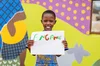 Image of a young child holding up a poster with the word ‘enganit’ written in green and red ink.