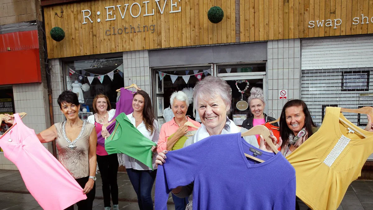 A group of women are smiling holding up clothes in front of the R:evolve store.