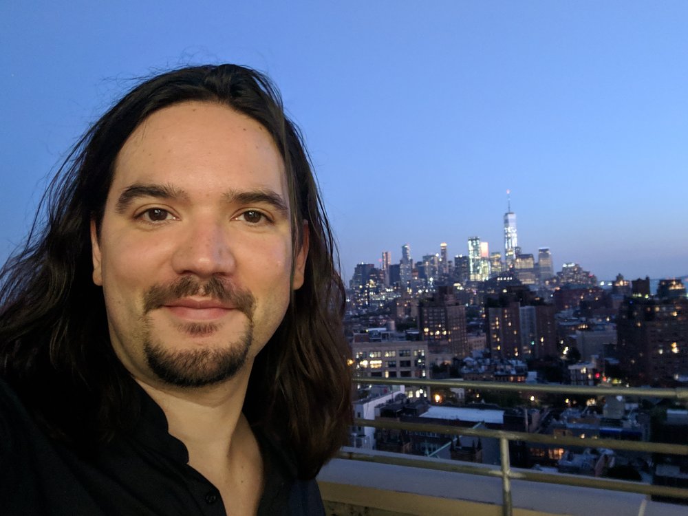 Ricardo smiles on the rooftop of Google’s New York City office, with the lower Manhattan night skyline in the background.