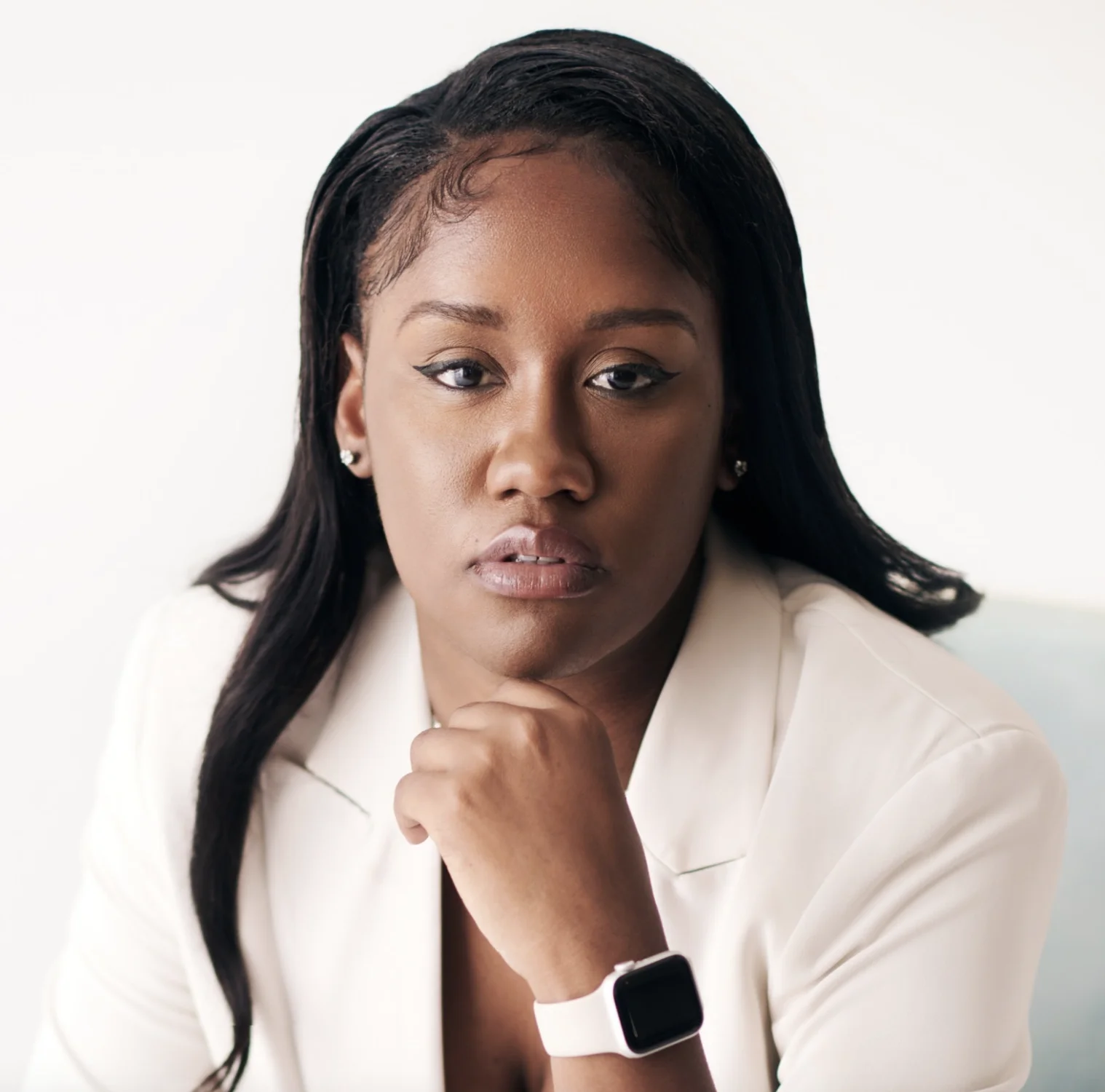 Rishielle Giscombe stares directly into the camera with her chin resting on her hand. She is wearing a cream blazer and watch.