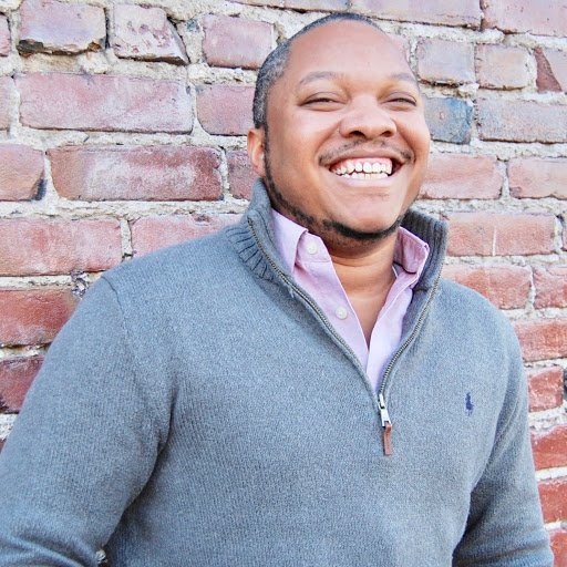 Headshot of Rodney Foxworth laughing in front of a red brick wall.