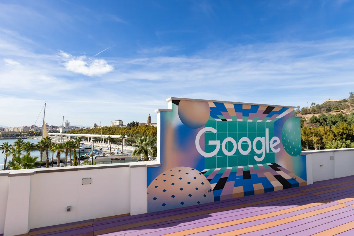 Ein Google Schriftzug auf einer bunten Wand, im Hintergrund ist ein Hafen zu sehen