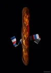 A photograph of a baguette on a black background against a wide, blue, red and white striped ribbon