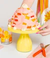 Sam’s pink Jell-O crown cake has red and orange fruit chunks and white balls of cream. It sits atop a yellow cake stand.