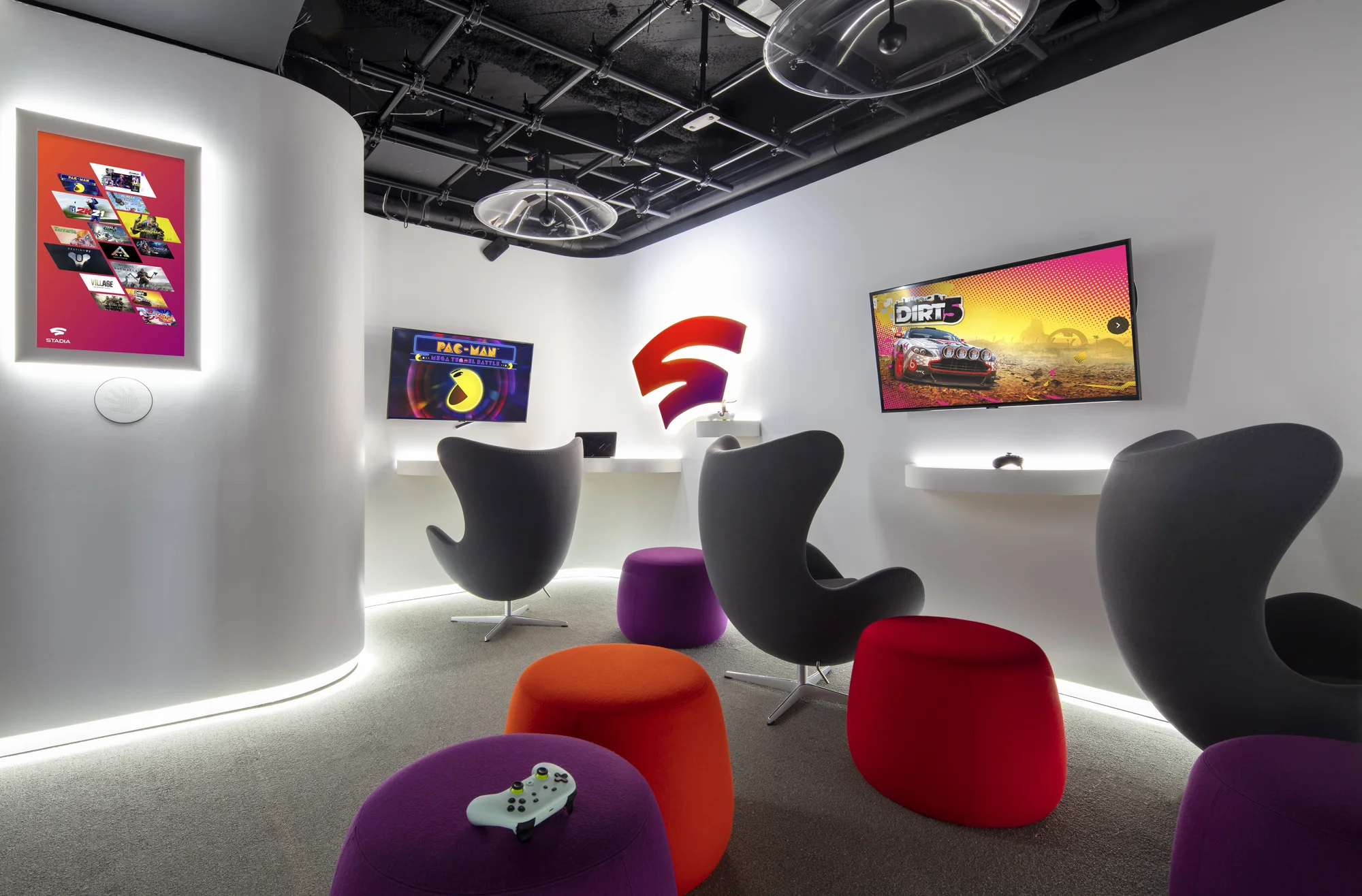 Chairs and ottomans stand in a room with screens to play Stadia games on.