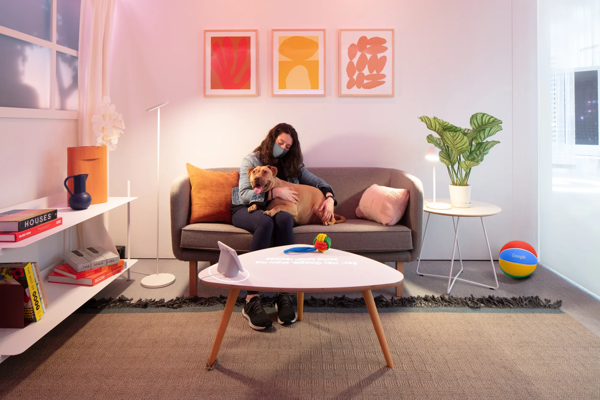 A person sits on a couch with a dog in a living room outfitted with Nest products.