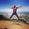 Reza jumping outdoors with a city behind him