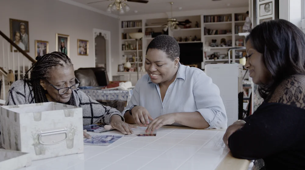 Three Black women sit at a table looking at photographs. Video shows a Local Guide on Google Maps showcasing Black history landmarks in New Orleans.