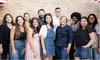 A group of people standing against a brick wall, all looking into the camera and smiling.